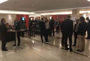 Groups of people in business attire stand and talk in a spacious, modern lobby with red walls and marble flooring at the BoostAerospace corporate headquarters.