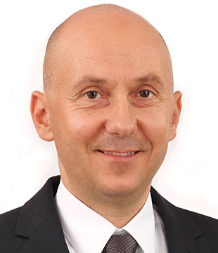 A middle-aged man in a suit, dress shirt, and tie is smiling at the camera against a plain white background, ready to present his Technical Review.