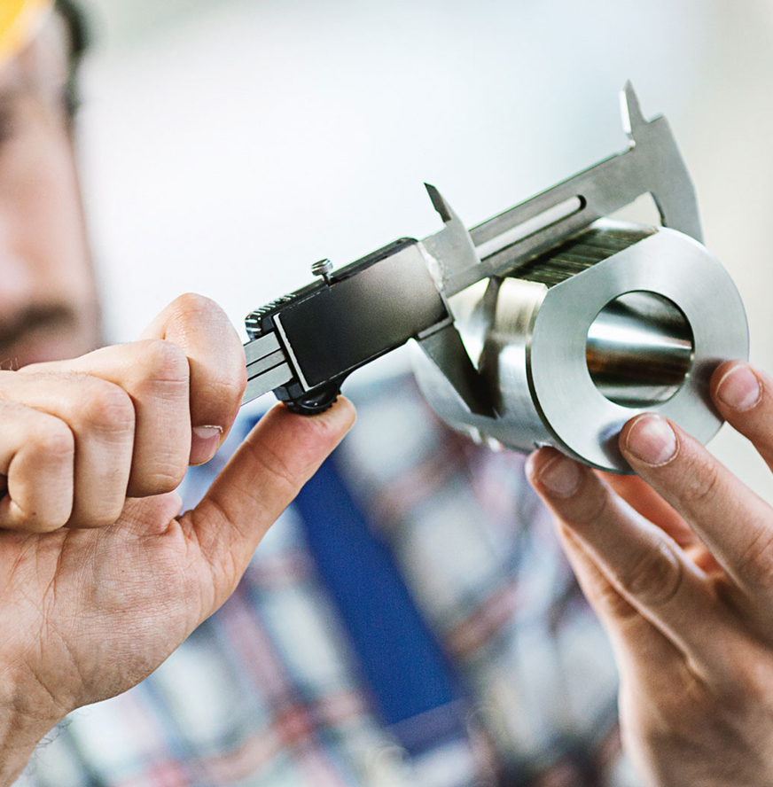 A person uses a caliper to measure the diameter of a cylindrical metal part.