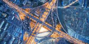 Aerial view of a large, illuminated highway interchange with multiple roads, ramps, and surrounding urban buildings at night.